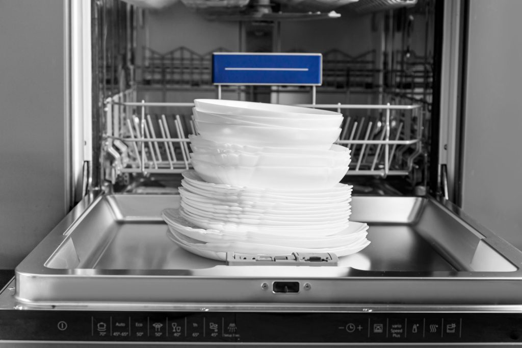 A stack of plates standing on the lowered door of a dishwasher