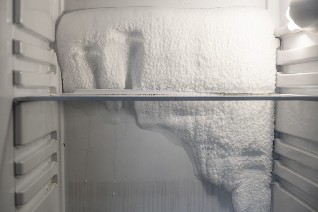 A thick slab of frost grown across the back wall and shelf of a freezer