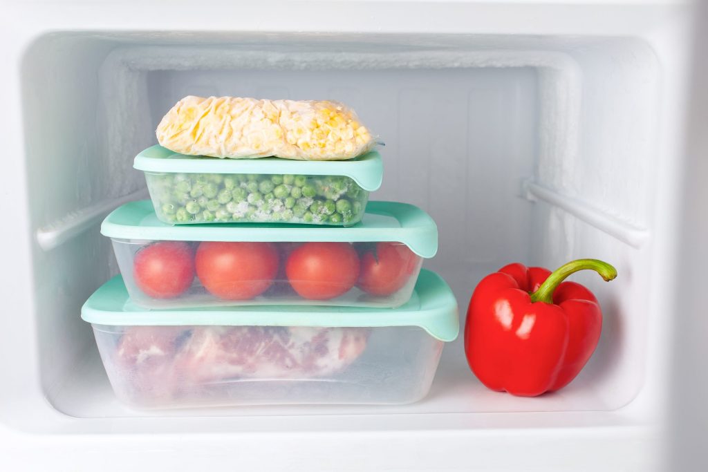 Stacked containers of frozen vegetables and meat in a white freezer compartment