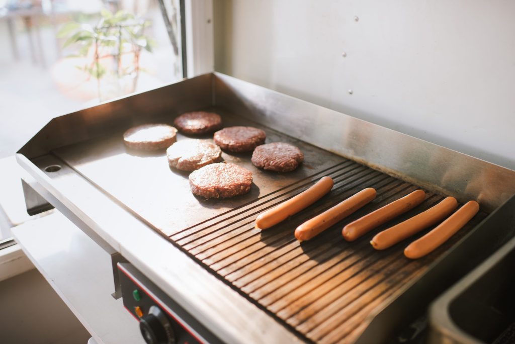 Burgers on a flat griddle plate beside hot dogs on the grill grates