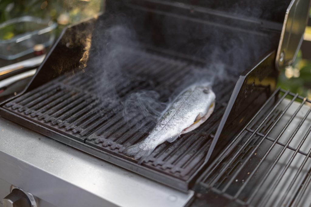 A fish steaming on one side of a grill's grates while the other side sits empty