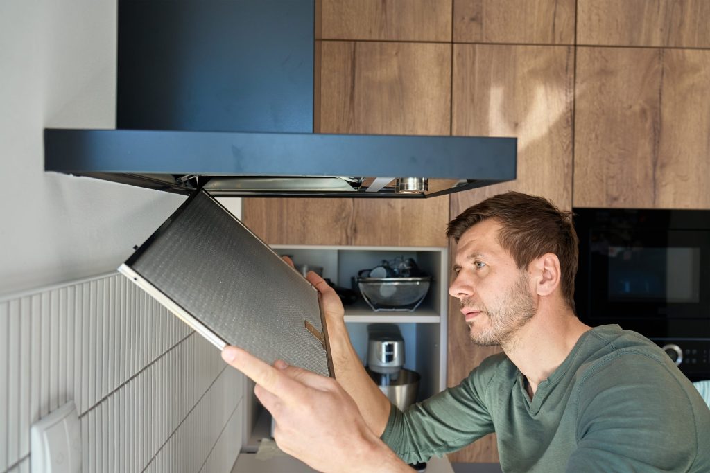 A man lifting a mesh filter out of an island hood