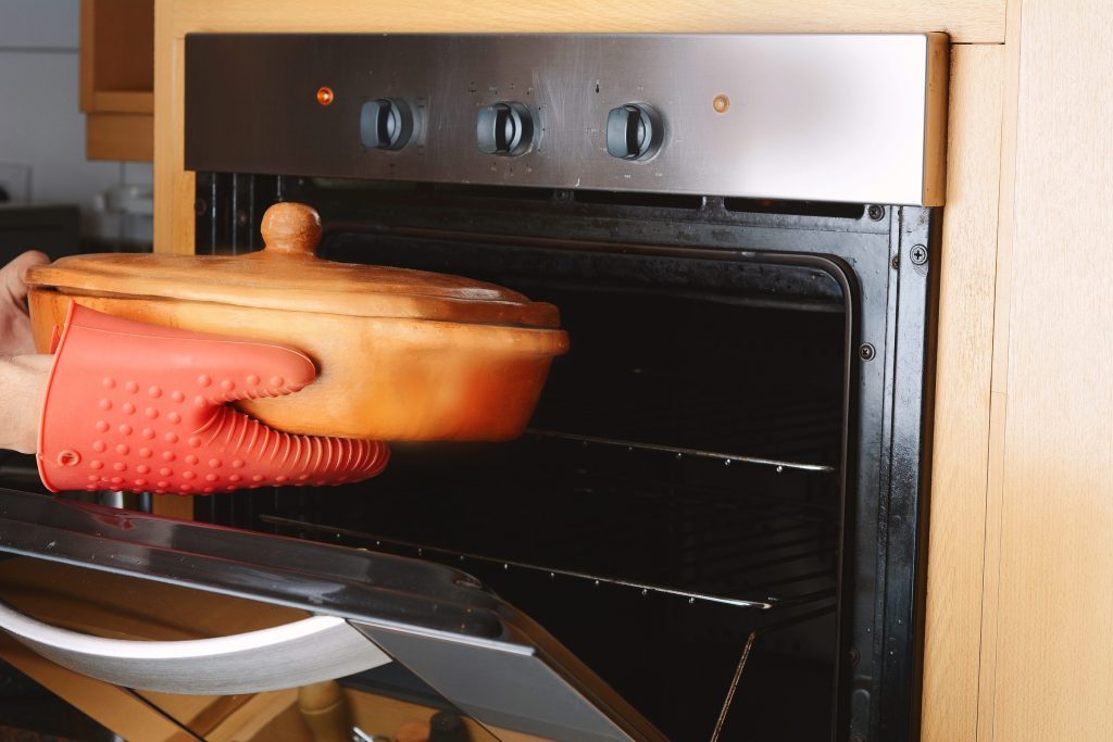A gloved hand setting a covered dish onto the rack of a hot oven