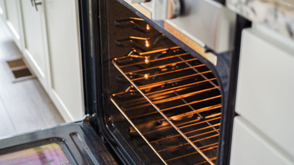 A built-in oven standing open, its door down and the cavity lamp lit on empty racks