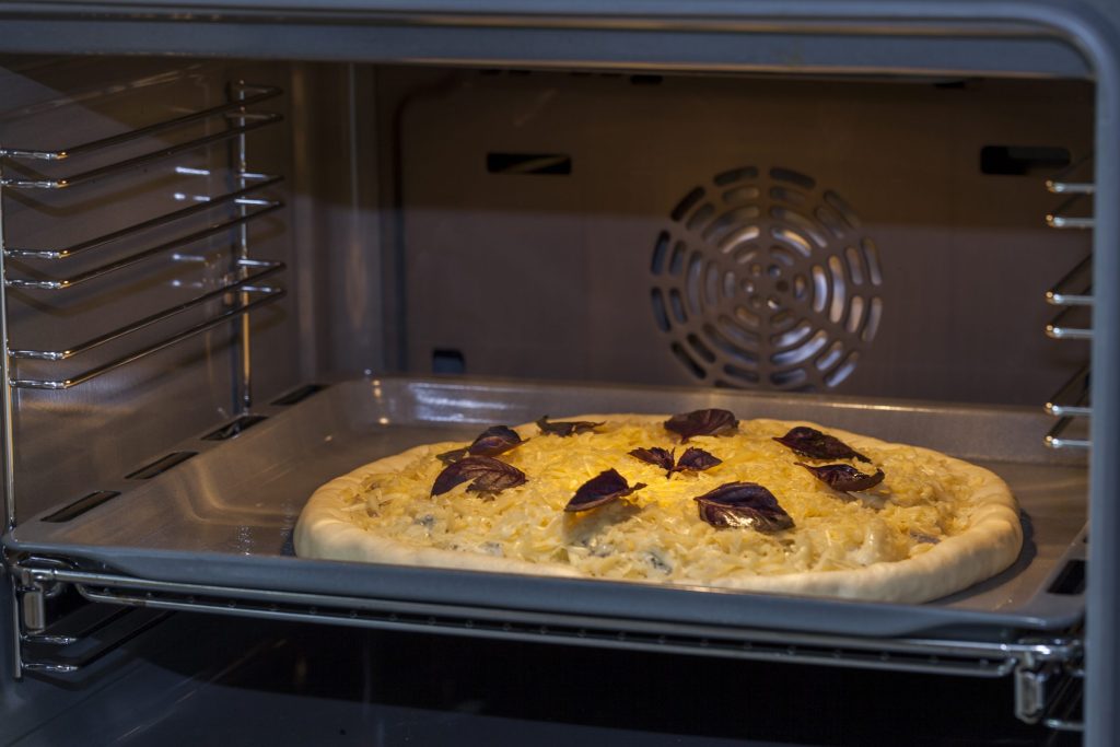 A pizza on a tray on the middle rack of an oven, the fan cover behind it