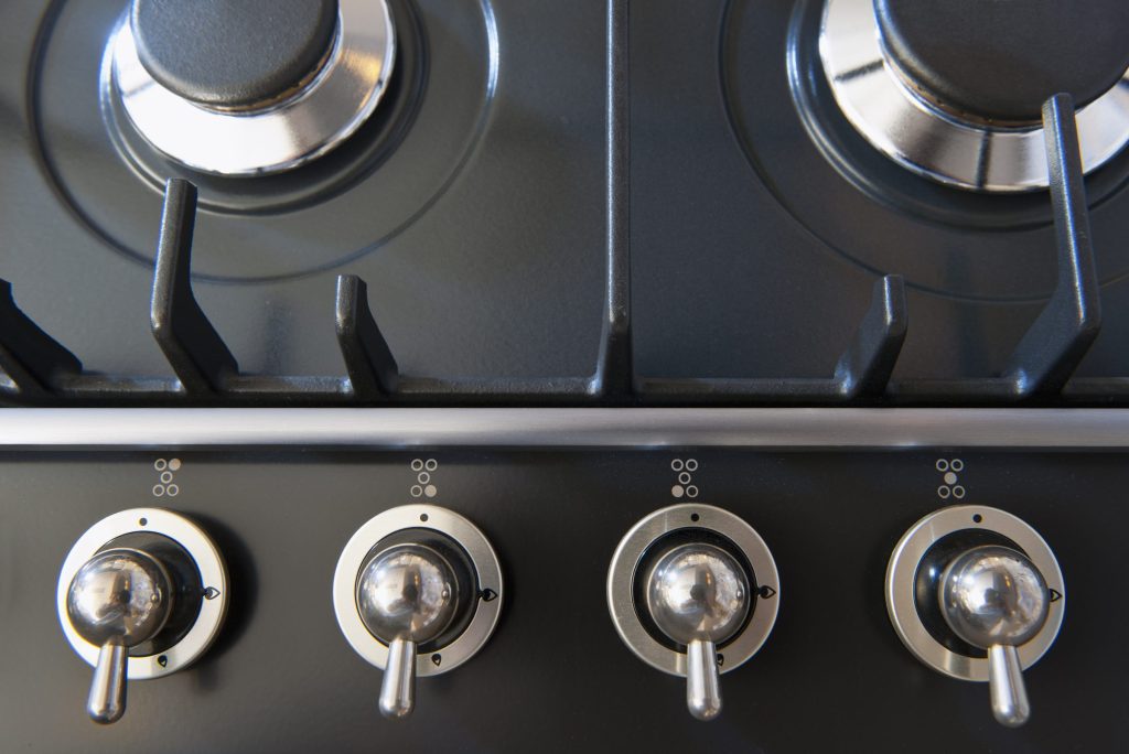 Four lever knobs in a row below the burners of a dark range