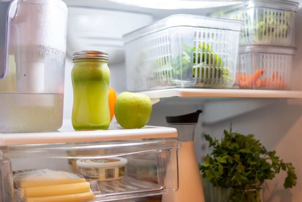 A filter jug and a bottled drink on the shelf of an open refrigerator beside crisper baskets