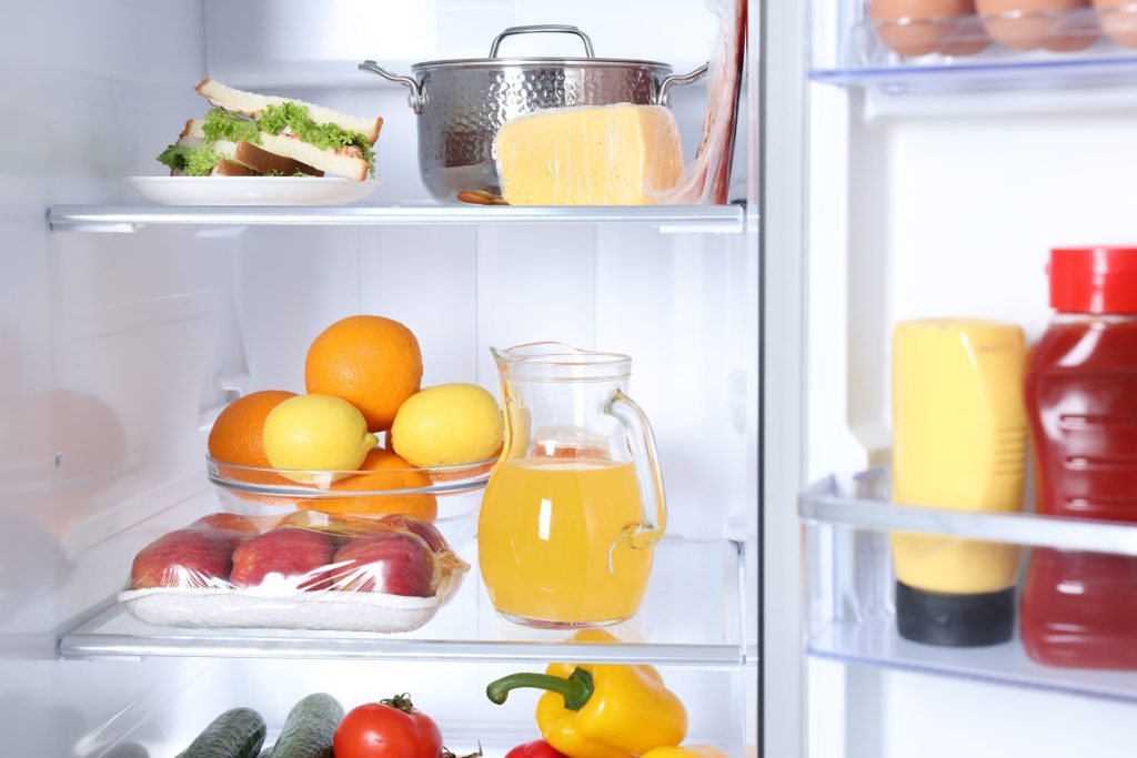 An open refrigerator with fruit, a jug of juice and a full door shelf
