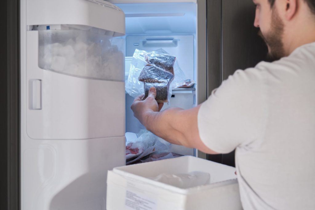 A man putting packaged food onto the shelves of an open refrigerator