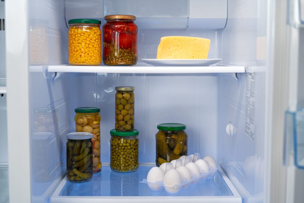A refrigerator standing open on shelves of jars, cheese and eggs