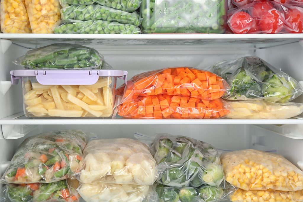 Three packed shelves inside a freezer column, bagged vegetables stacked front to back