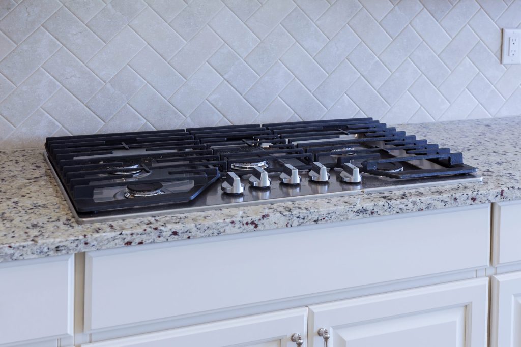 A wide five-burner gas cooktop set into a granite counter above white cabinetry