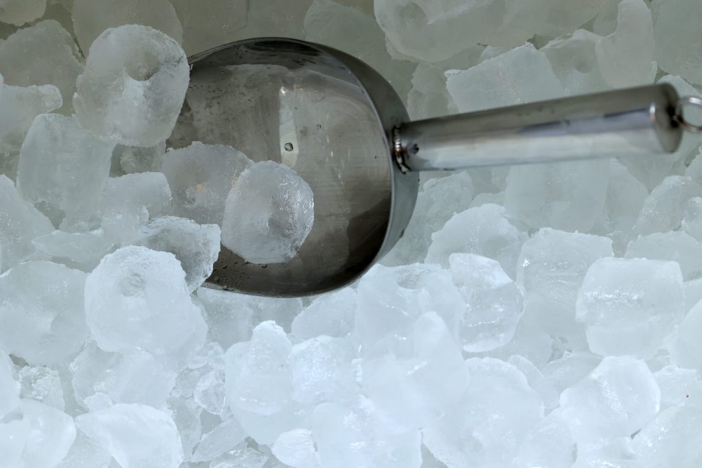 A metal scoop resting in a bin of clear machine-made ice