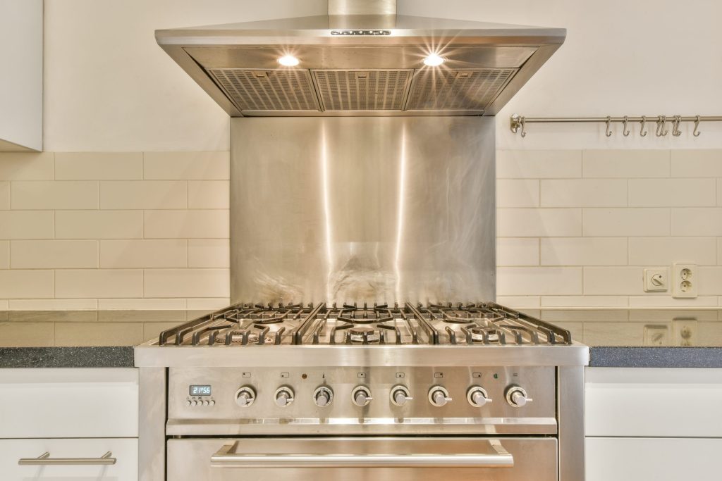 A stainless professional gas range with eight knobs and cast grates, built into a white kitchen run