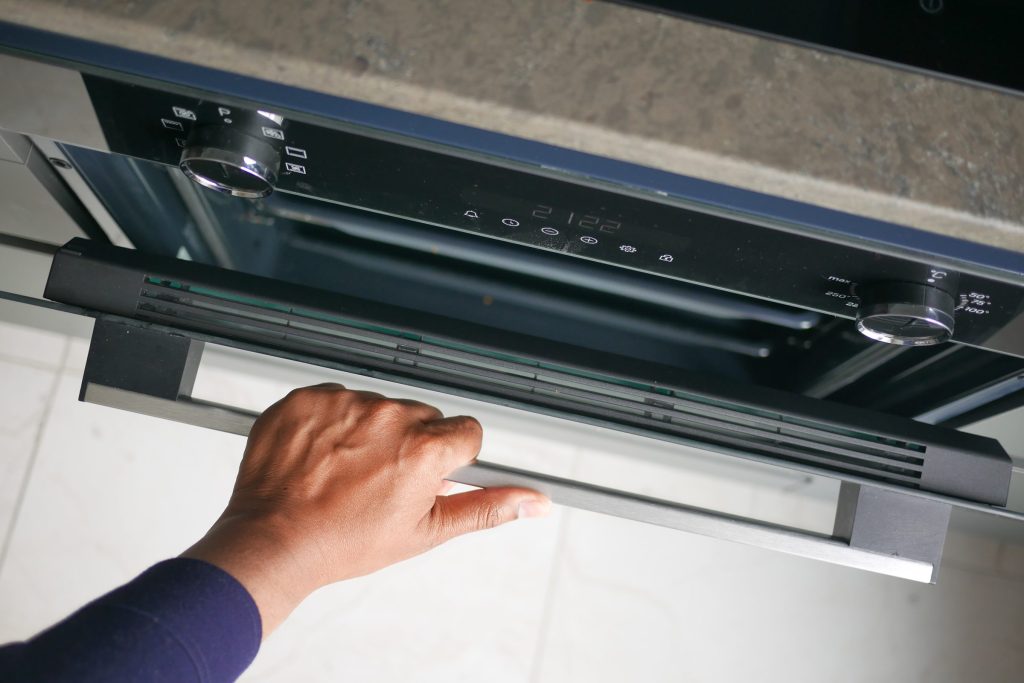 A hand drawing out the glass visor of a slimline extractor hood to reach its filters