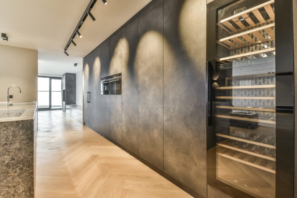 A tall glass-fronted wine cabinet integrated into a dark cabinetry run, lit from inside